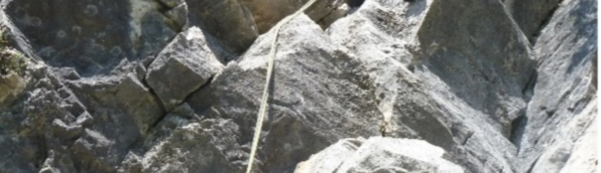 Eine Person seilt sich an einer steilen, zerklüfteten Felswand mit Sicherung ab. | © DAV Dortmund