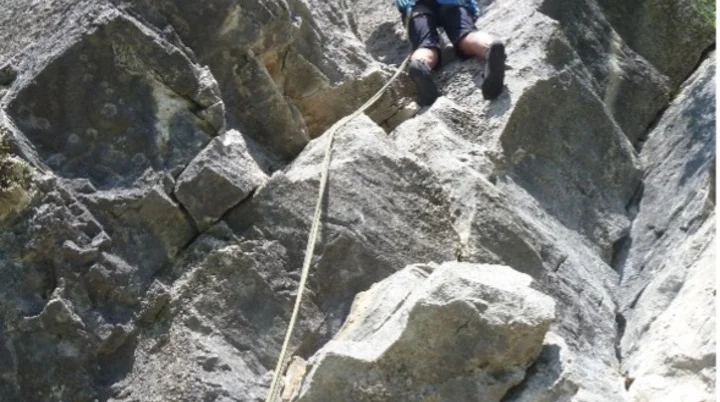 Eine Person seilt sich an einer steilen, zerklüfteten Felswand mit Sicherung ab. | © DAV Dortmund