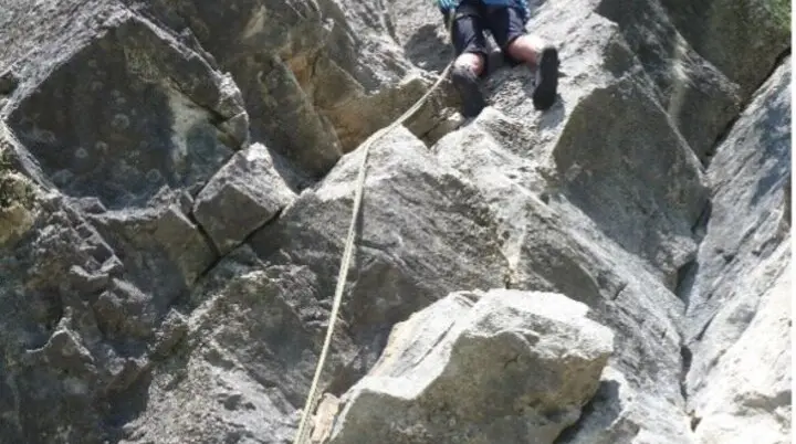 Eine Person seilt sich an einer steilen, zerklüfteten Felswand mit Sicherung ab. | © DAV Dortmund