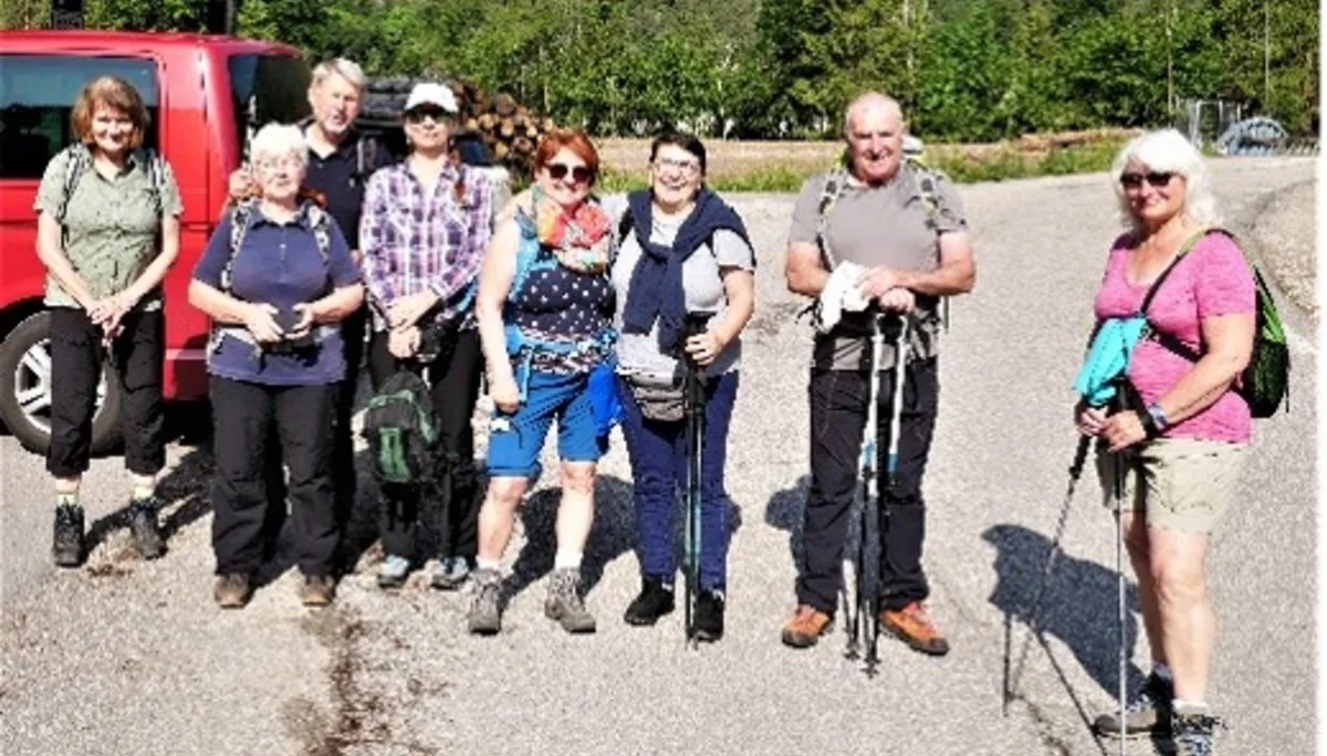 Eine Gruppe älterer Wander*innen steht mit Wanderstöcken und Rucksäcken auf einem Parkplatz, bereit für eine Tour. | © DAV Dortmund