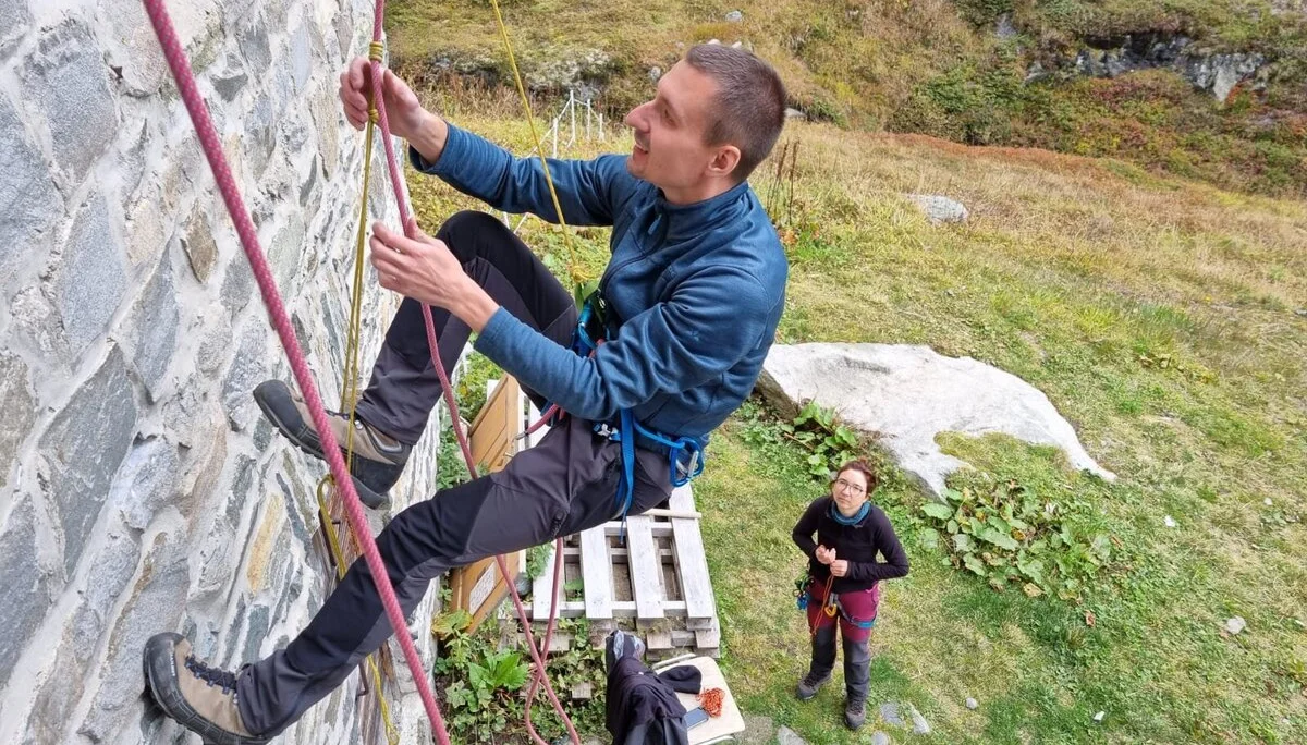 Eine Person übt an einer Hauswand mit Kletterseil und Gurt, eine zweite Person sichert am Boden. | © DAV Dortmund