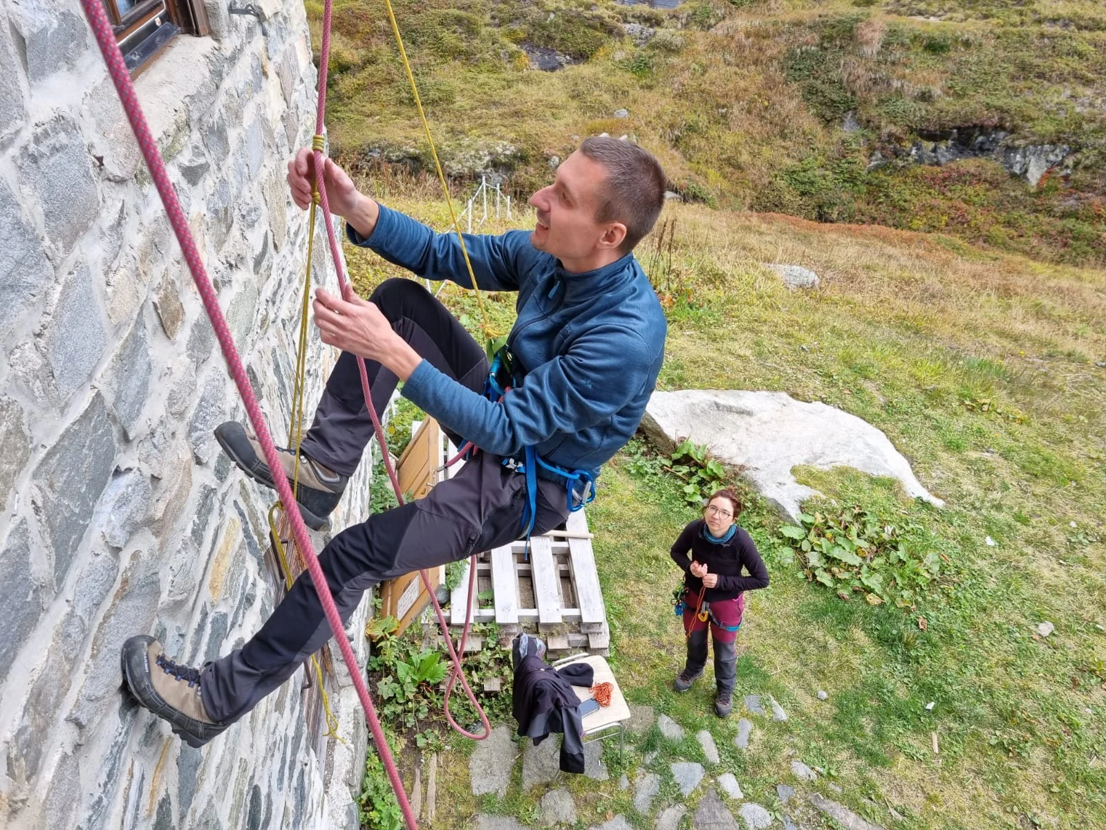 Eine Person übt an einer Hauswand mit Kletterseil und Gurt, eine zweite Person sichert am Boden. | © DAV Dortmund