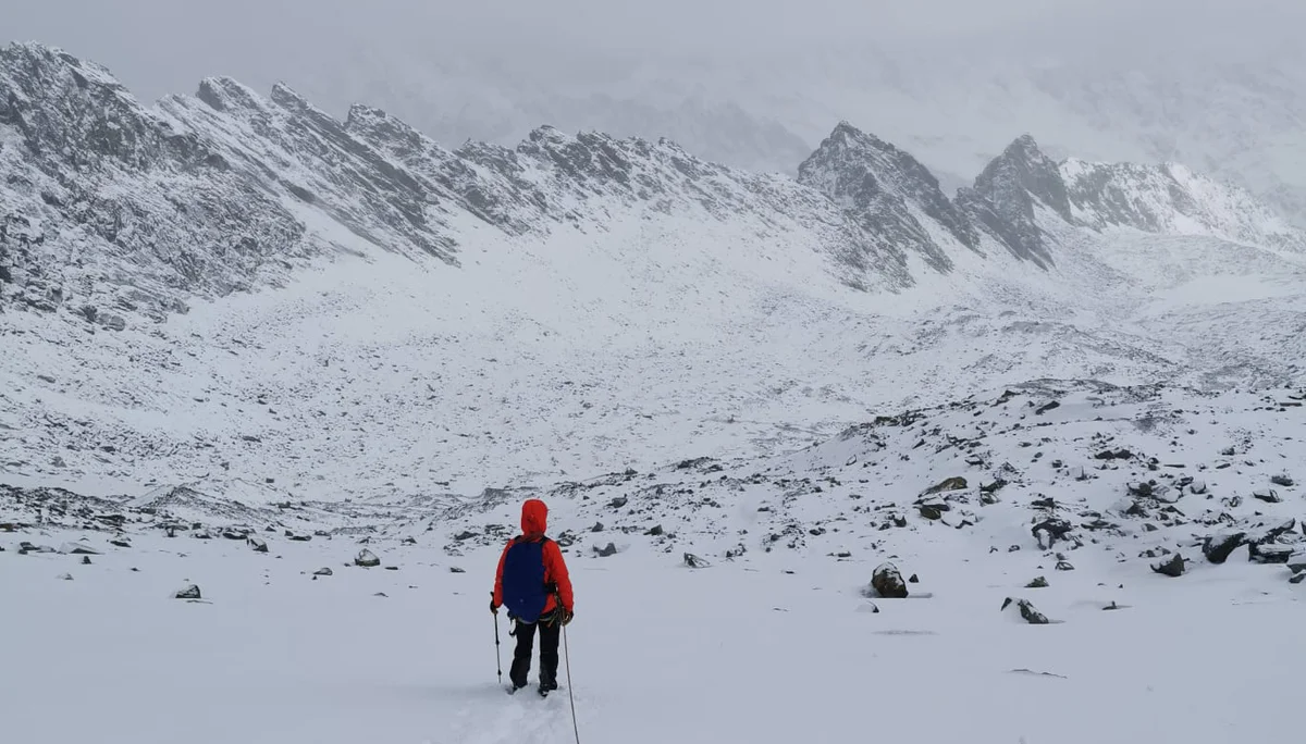 Eine Person in oranger Jacke geht allein auf einer Spur durch verschneites Hochgebirge, umgeben von Nebel. | © DAV Dortmund