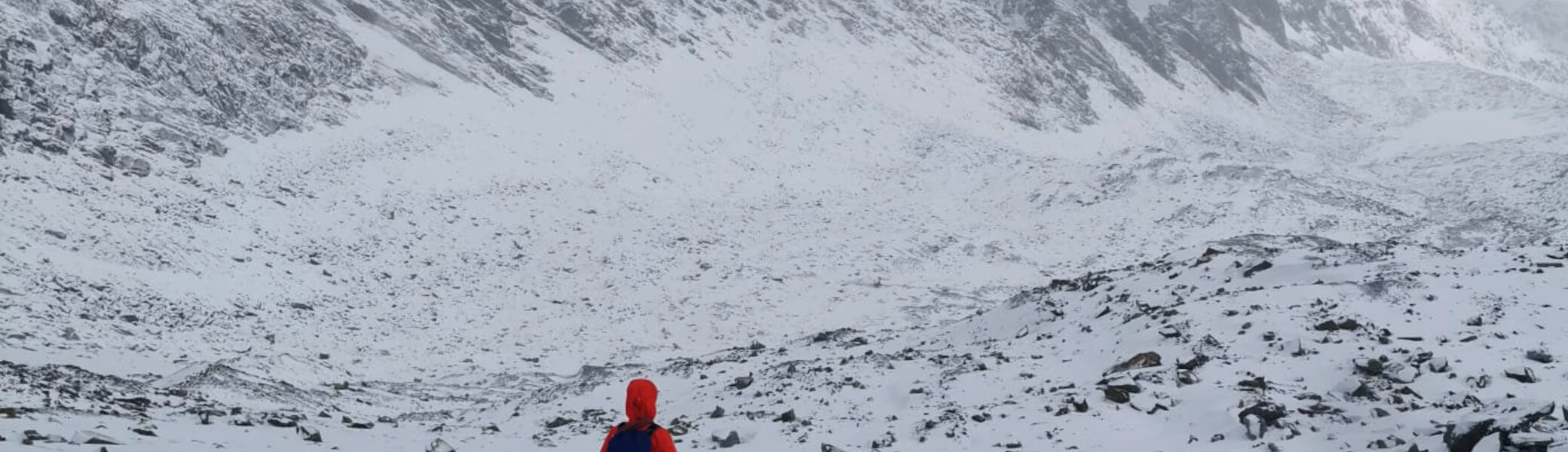 Eine Person in oranger Jacke geht allein auf einer Spur durch verschneites Hochgebirge, umgeben von Nebel. | © DAV Dortmund