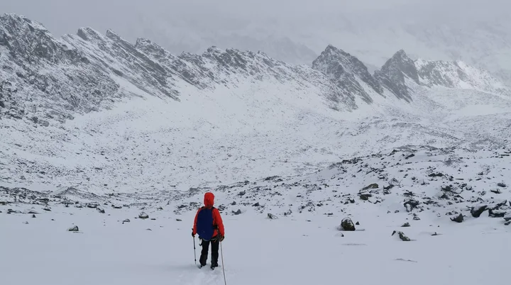 Eine Person in oranger Jacke geht allein auf einer Spur durch verschneites Hochgebirge, umgeben von Nebel. | © DAV Dortmund
