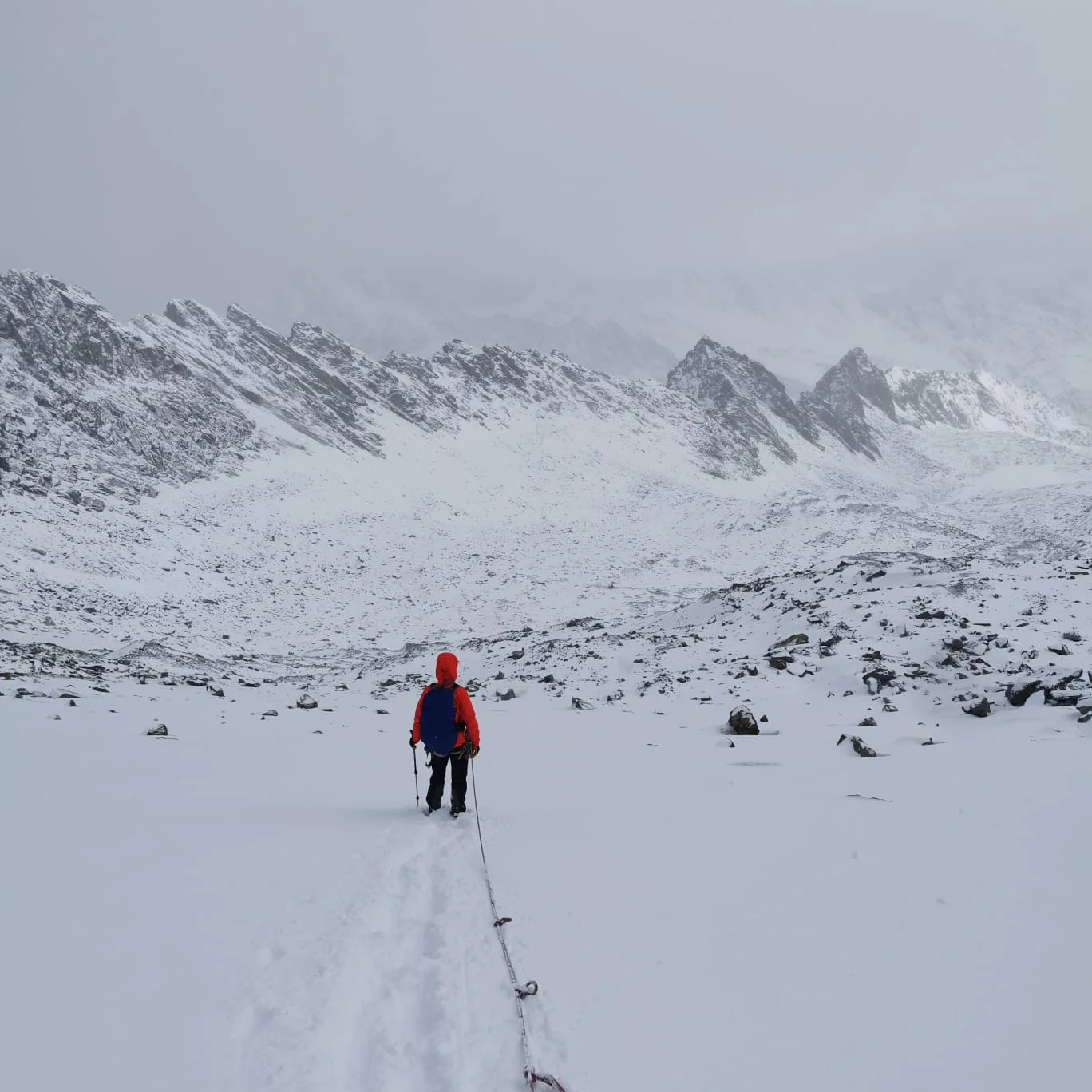 Eine Person in oranger Jacke geht allein auf einer Spur durch verschneites Hochgebirge, umgeben von Nebel. | © DAV Dortmund