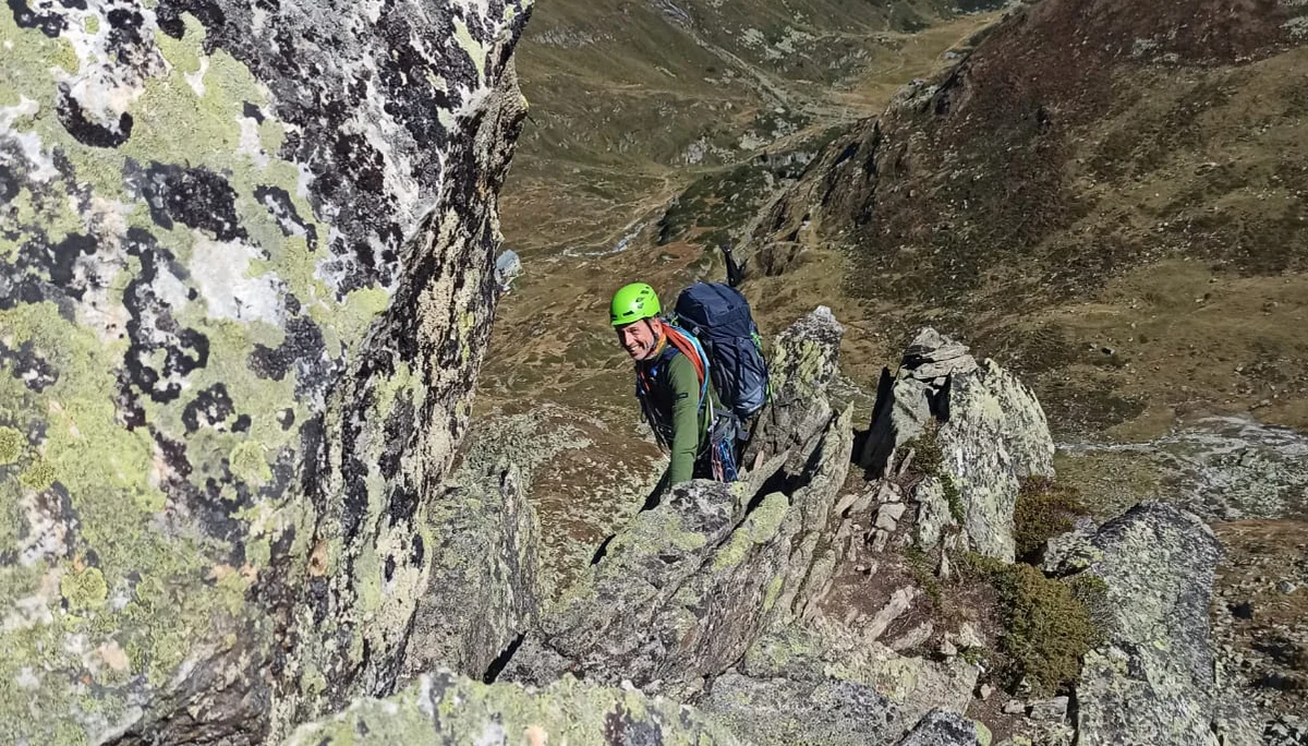 Eine Person mit Helm und Rucksack klettert in alpinem Gelände über einen felsigen Grat. | © DAV Dortmund