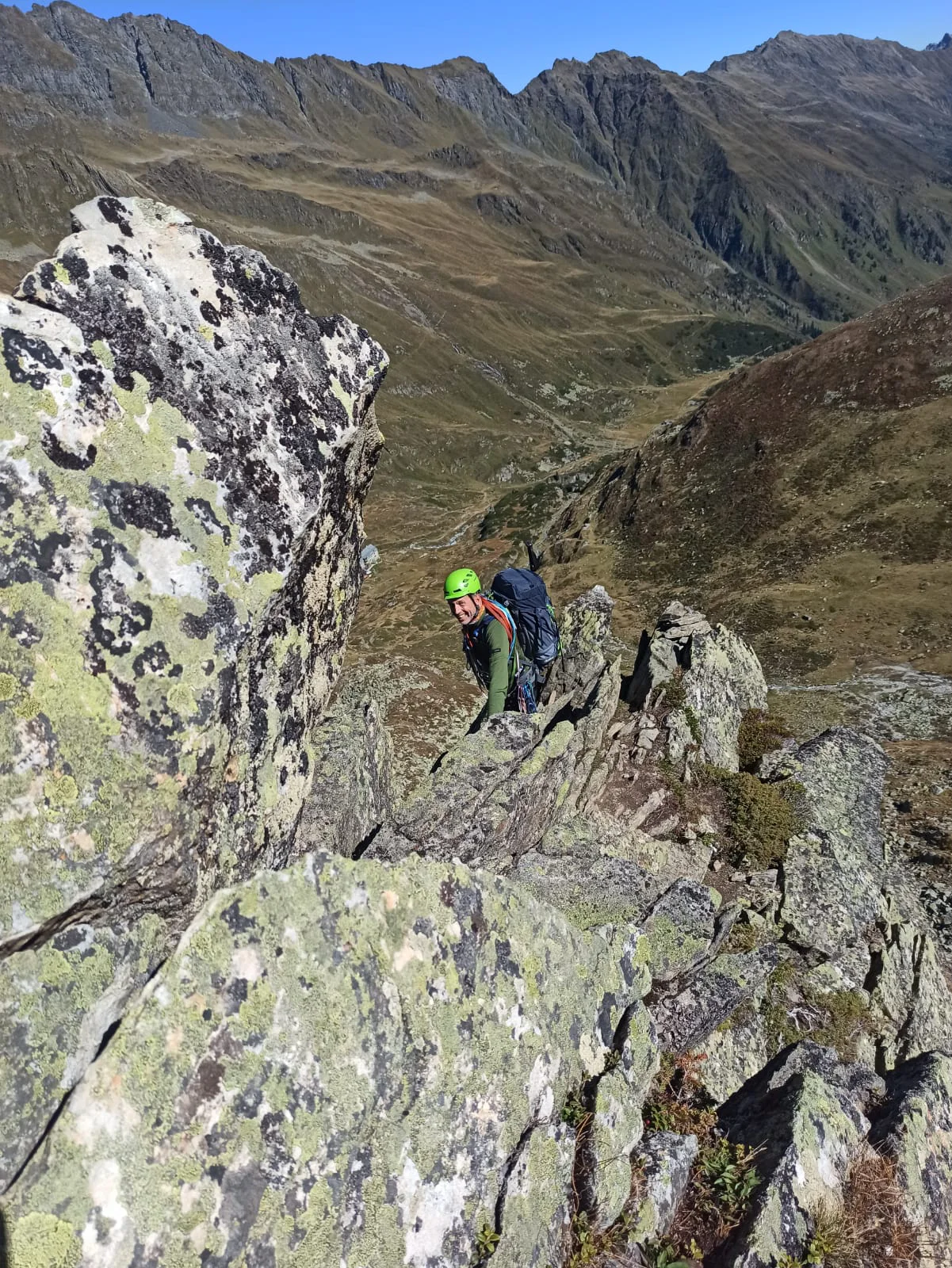 Eine Person mit Helm und Rucksack klettert in alpinem Gelände über einen felsigen Grat. | © DAV Dortmund