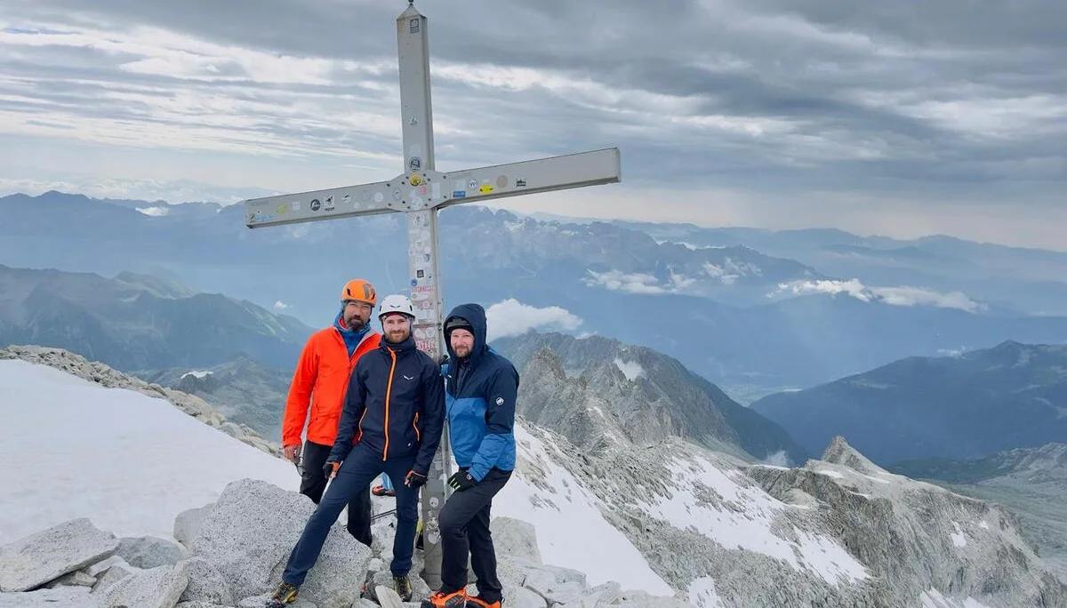 Vier Bergsteiger stehen neben einem Gipfelkreuz auf felsigem Terrain mit Aussicht auf ein Gebirge. | © DAV Dortmund