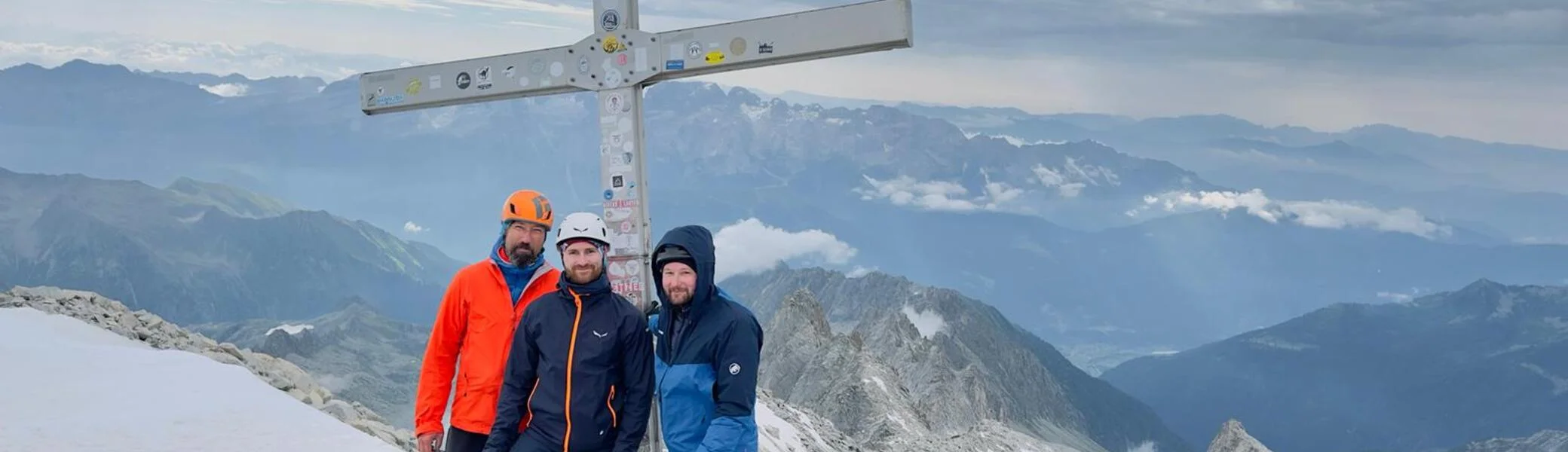 Vier Bergsteiger stehen neben einem Gipfelkreuz auf felsigem Terrain mit Aussicht auf ein Gebirge. | © DAV Dortmund