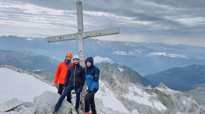 Vier Bergsteiger stehen neben einem Gipfelkreuz auf felsigem Terrain mit Aussicht auf ein Gebirge. | © DAV Dortmund
