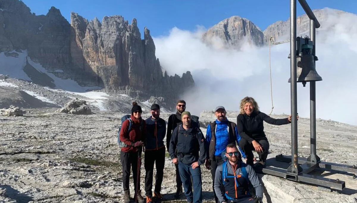 Eine Wandergruppe steht vor felsiger Kulisse mit Glocke in den Dolomiten. | © DAV Dortmund
