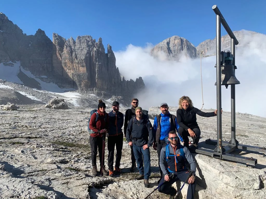 Eine Wandergruppe steht vor felsiger Kulisse mit Glocke in den Dolomiten. | © DAV Dortmund