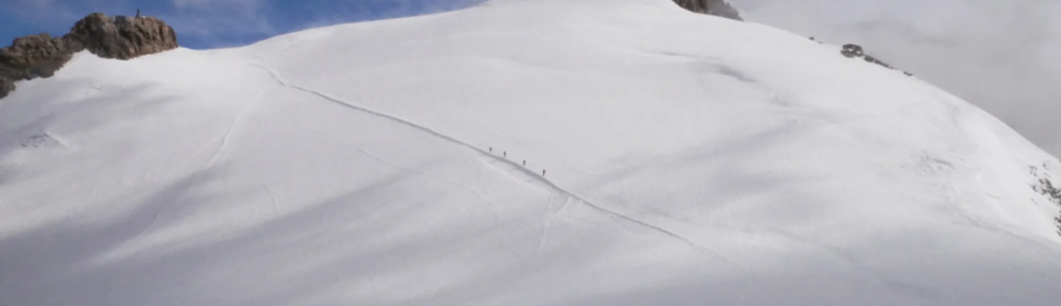 Zwei Bergsteiger*innen gehen über ein verschneites Gletscherfeld auf einen Gipfel zu. | © DAv Dortmund