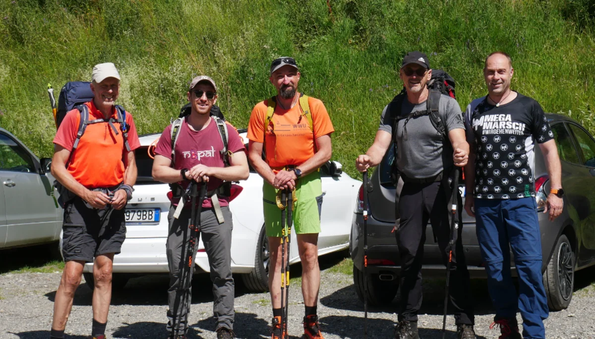 Fünf Wanderer mit Stöcken stehen bereit auf einem Parkplatz vor grünen Hügeln. | © DAV Dortmund