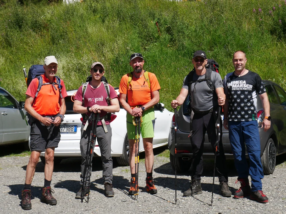 Fünf Wanderer mit Stöcken stehen bereit auf einem Parkplatz vor grünen Hügeln. | © DAV Dortmund