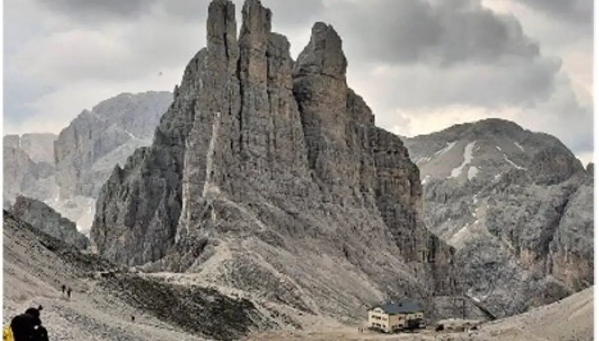 Große Felsformationen ragen auf, darunter eine kleine Berghütte, dramatische Wolken im Hintergrund. | © DAV Dortmund