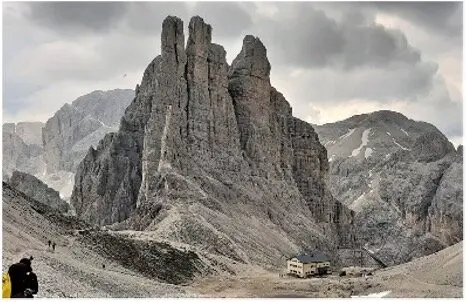 Große Felsformationen ragen auf, darunter eine kleine Berghütte, dramatische Wolken im Hintergrund. | © DAV Dortmund