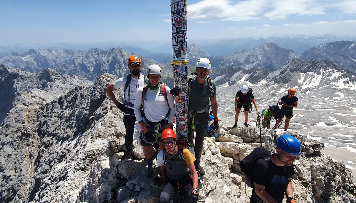 Eine Gruppe Bergsteiger*innen steht am Gipfelkreuz der Zugspitze mit Helm und Kletterausrüstung. | © DAV Dortmund