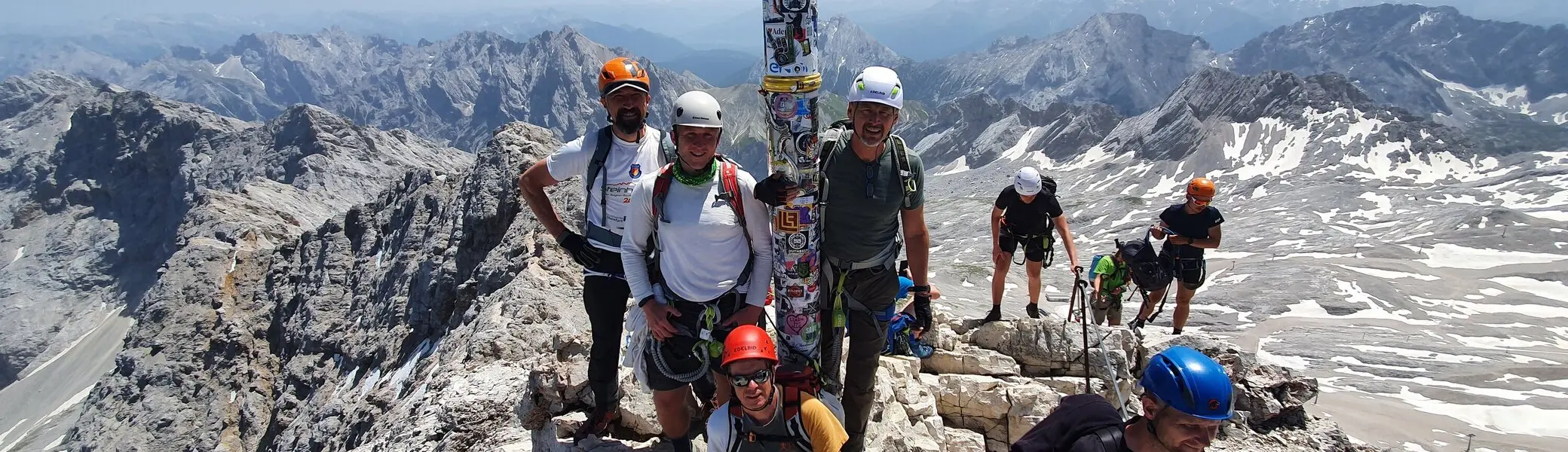 Eine Gruppe Bergsteiger*innen steht am Gipfelkreuz der Zugspitze mit Helm und Kletterausrüstung. | © DAV Dortmund