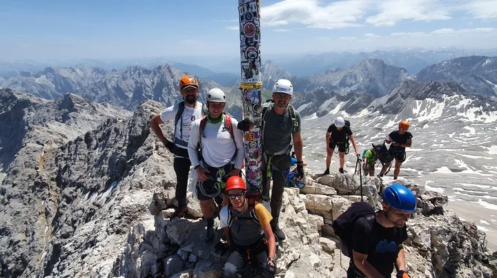 Eine Gruppe Bergsteiger*innen steht am Gipfelkreuz der Zugspitze mit Helm und Kletterausrüstung. | © DAV Dortmund