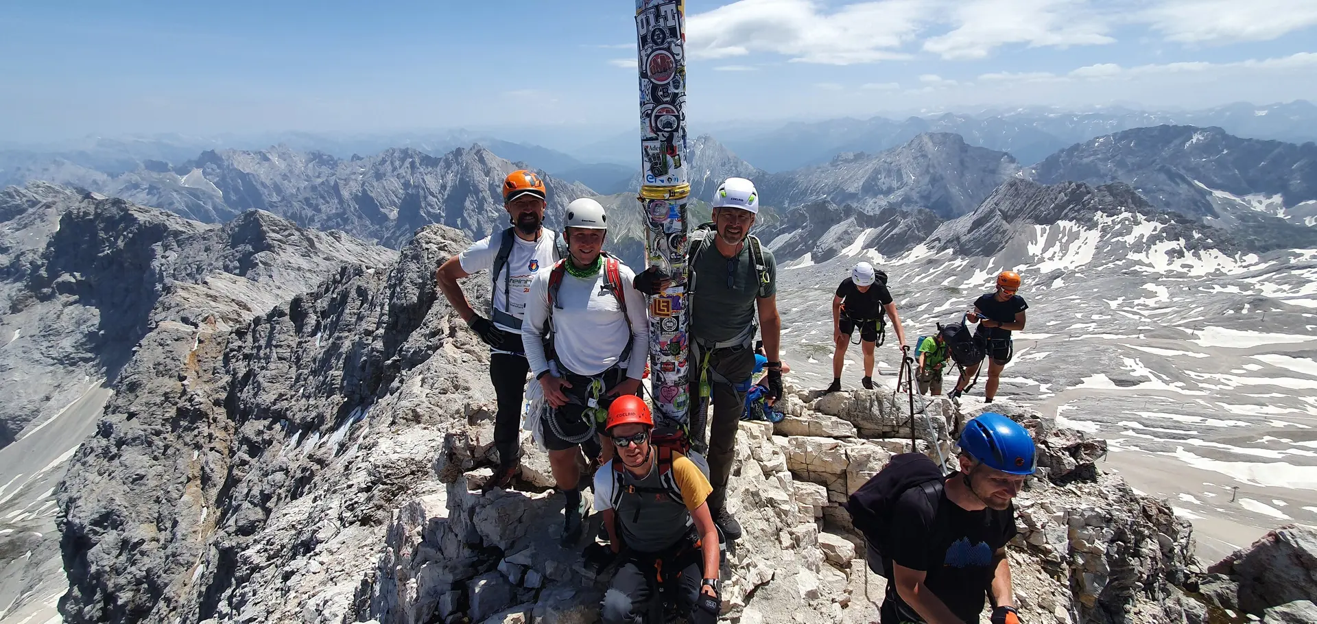 Eine Gruppe Bergsteiger*innen steht am Gipfelkreuz der Zugspitze mit Helm und Kletterausrüstung. | © DAV Dortmund