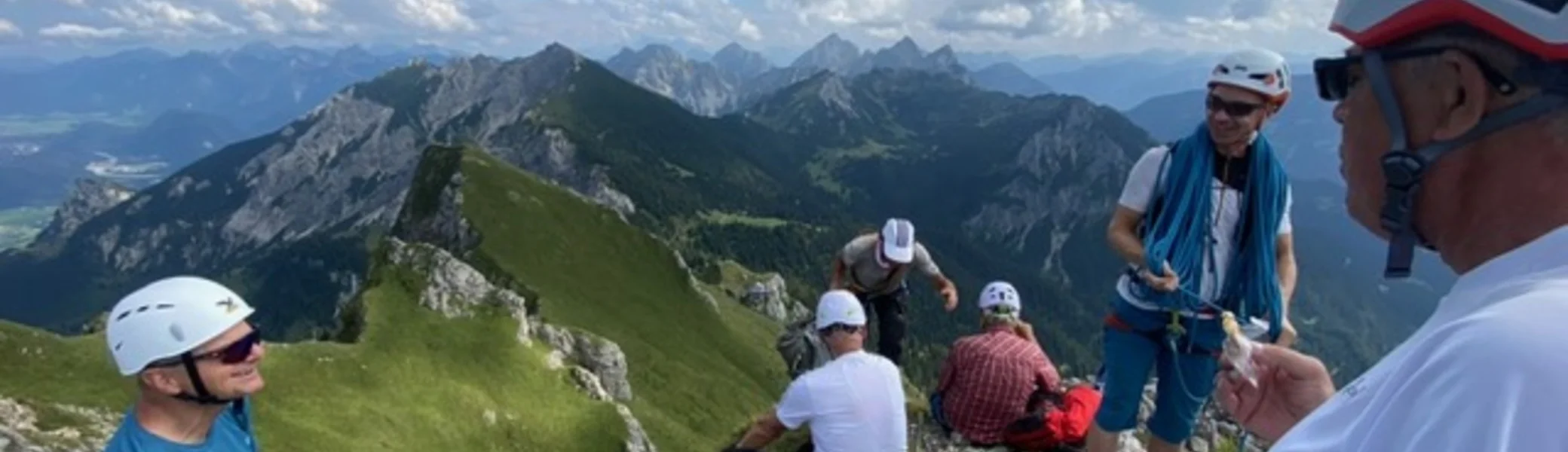 Gruppe mit Helmen und Kletterausrüstung sitzt am Gipfel mit Panoramablick. | © KD Schüler 