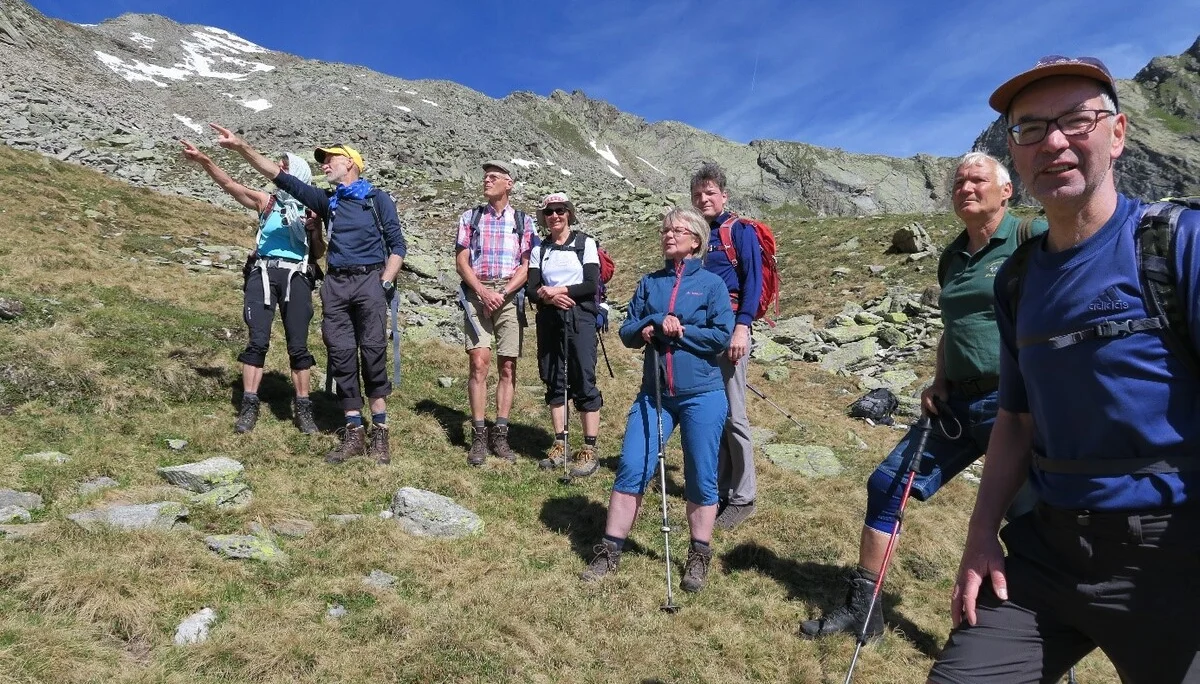 Eine Gruppe steht auf einer Bergwiese, einige zeigen in Richtung Gipfel, andere schauen entspannt. | © DAV Dortmund