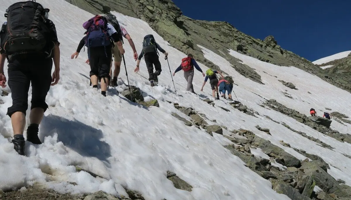 Eine Gruppe wandert über ein schräges Schneefeld zwischen Felsen unter blauem Himmel. | © DAV Dortmund