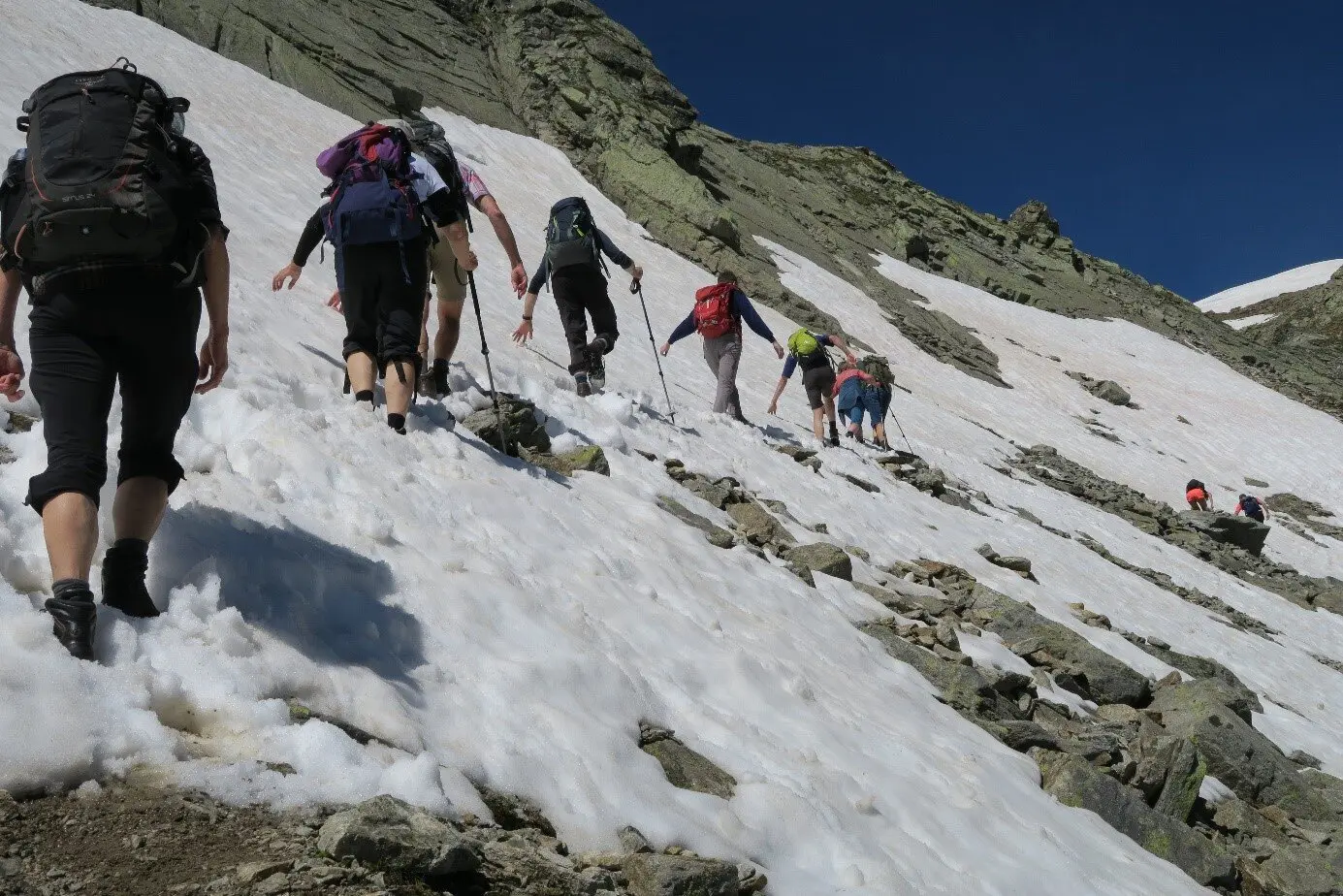 Eine Gruppe wandert über ein schräges Schneefeld zwischen Felsen unter blauem Himmel. | © DAV Dortmund
