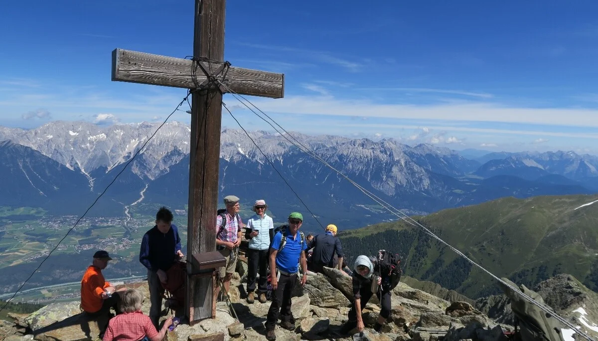 Eine größere Wandergruppe steht am Gipfelkreuz mit Blick auf das umliegende Alpenpanorama. | © DAV Dortmund
