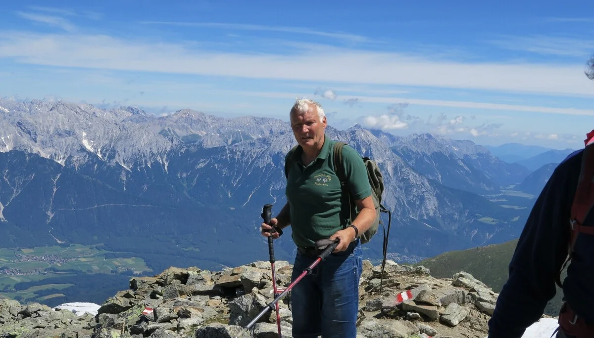 Ein älterer Mann mit Wanderstöcken steht auf felsigem Gipfelgelände mit Blick auf ein alpines Panorama. | © DAV Dortmund
