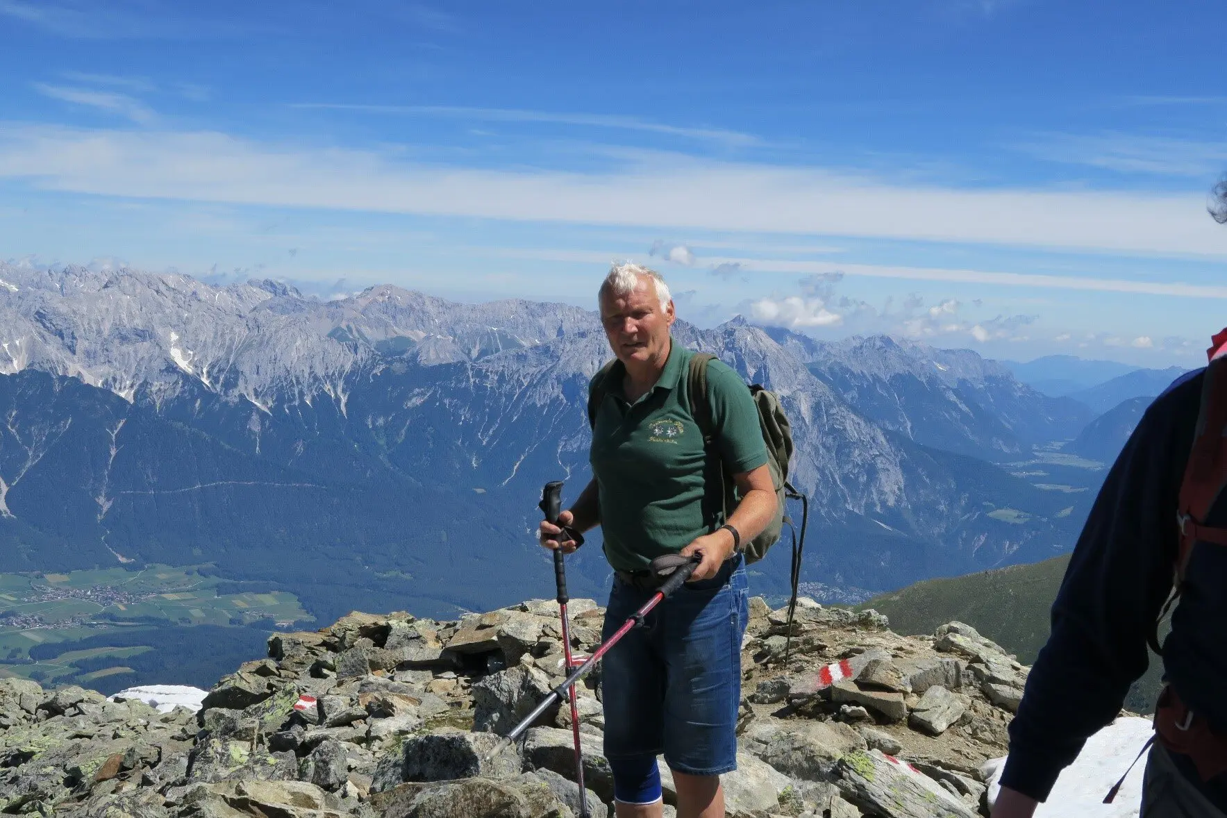 Ein älterer Mann mit Wanderstöcken steht auf felsigem Gipfelgelände mit Blick auf ein alpines Panorama. | © DAV Dortmund