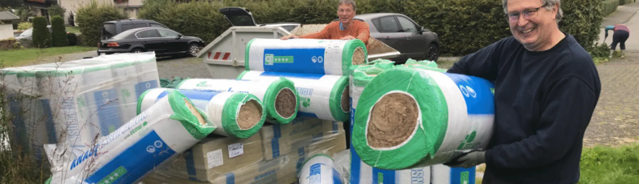 Ein Mann steht neben gestapelten Rollen Dämmmaterialien vor einem Haus in einem Dorf. | © DAV Dortmund