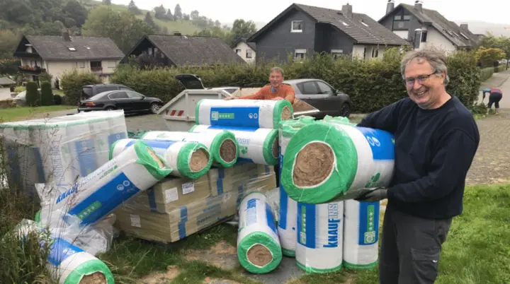 Ein Mann steht neben gestapelten Rollen Dämmmaterialien vor einem Haus in einem Dorf. | © DAV Dortmund