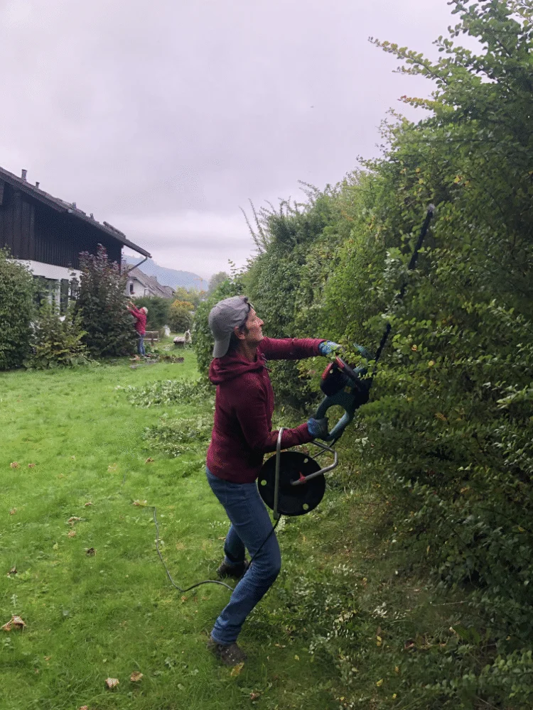 Eine Frau mit Motorsäge schneidet eine hohe Hecke im Garten neben einem Haus. | © DAV Dortmund