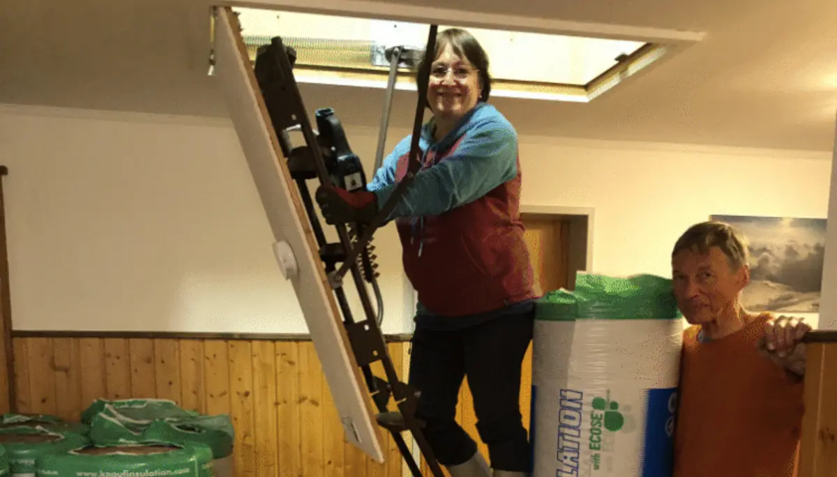 Zwei Personen reichen große Rollen Dämmmaterial durch eine geöffnete Dachluke. | © DAV Dortmund