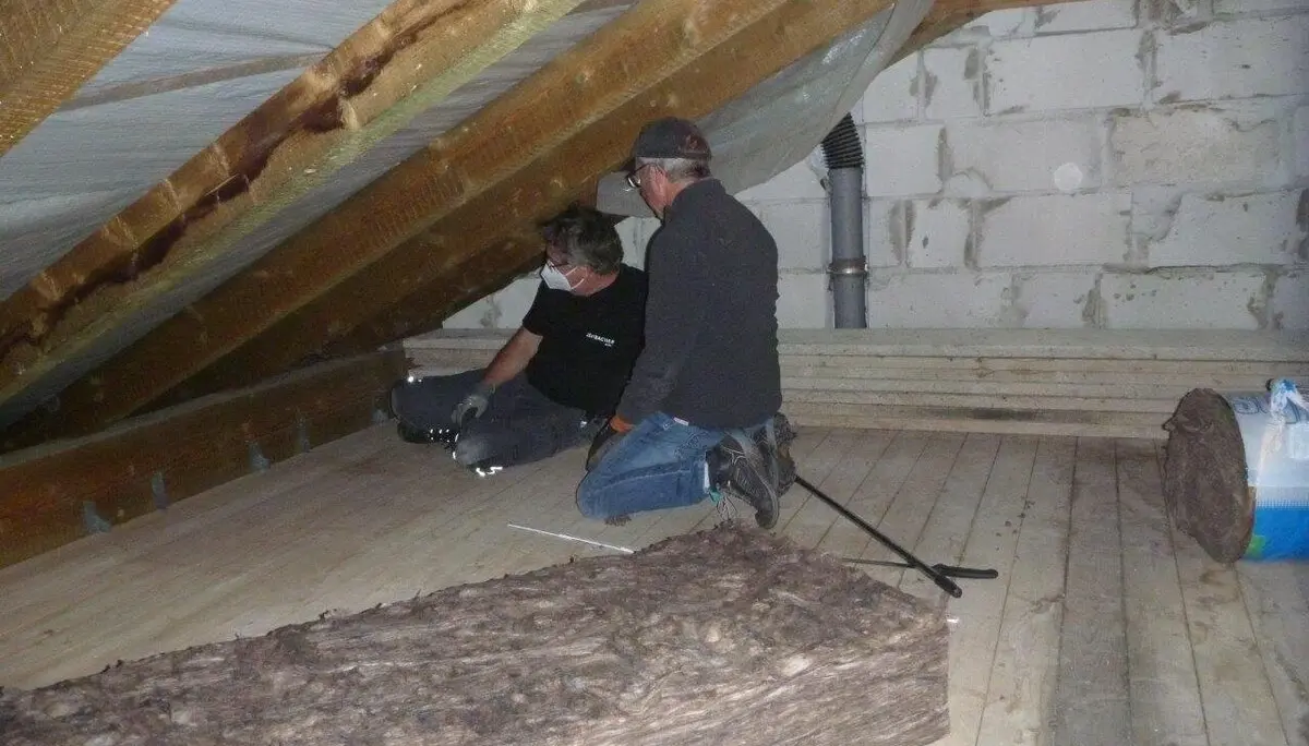 Zwei Männer verlegen Dämmmaterial im Dachboden eines Hauses mit sichtbaren Holzbalken. | © DAV Dortmund