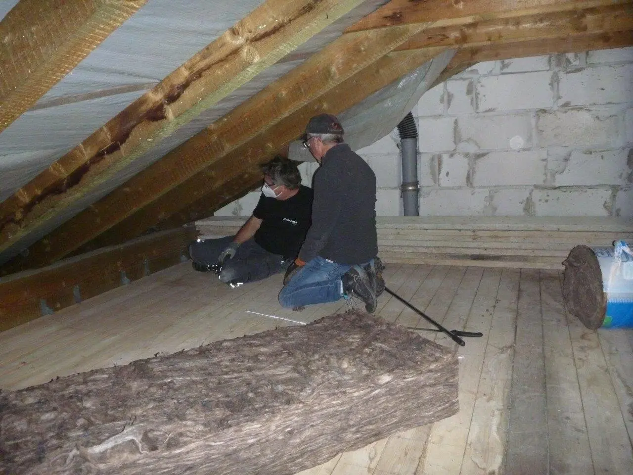 Zwei Männer verlegen Dämmmaterial im Dachboden eines Hauses mit sichtbaren Holzbalken. | © DAV Dortmund
