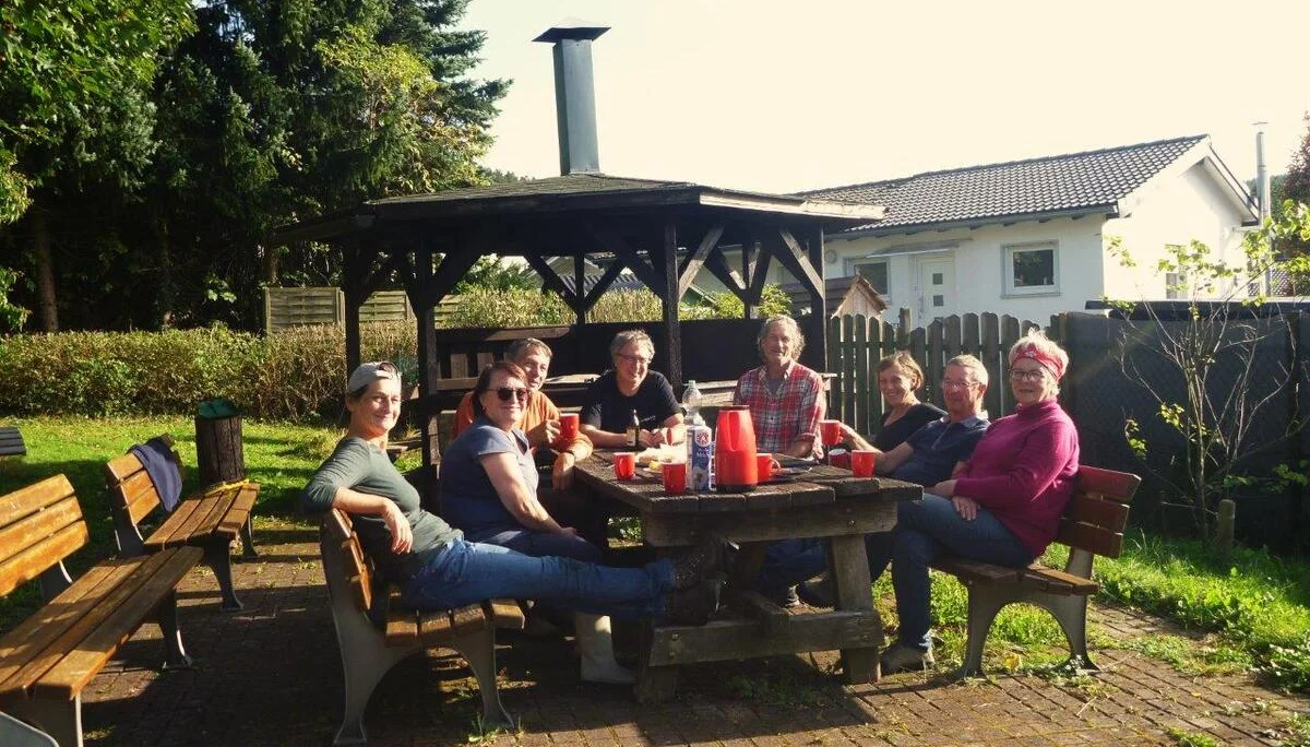 Sieben Personen sitzen gemütlich an einem Gartentisch bei Sonnenschein, Getränke auf dem Tisch. | © DAV Dortmund