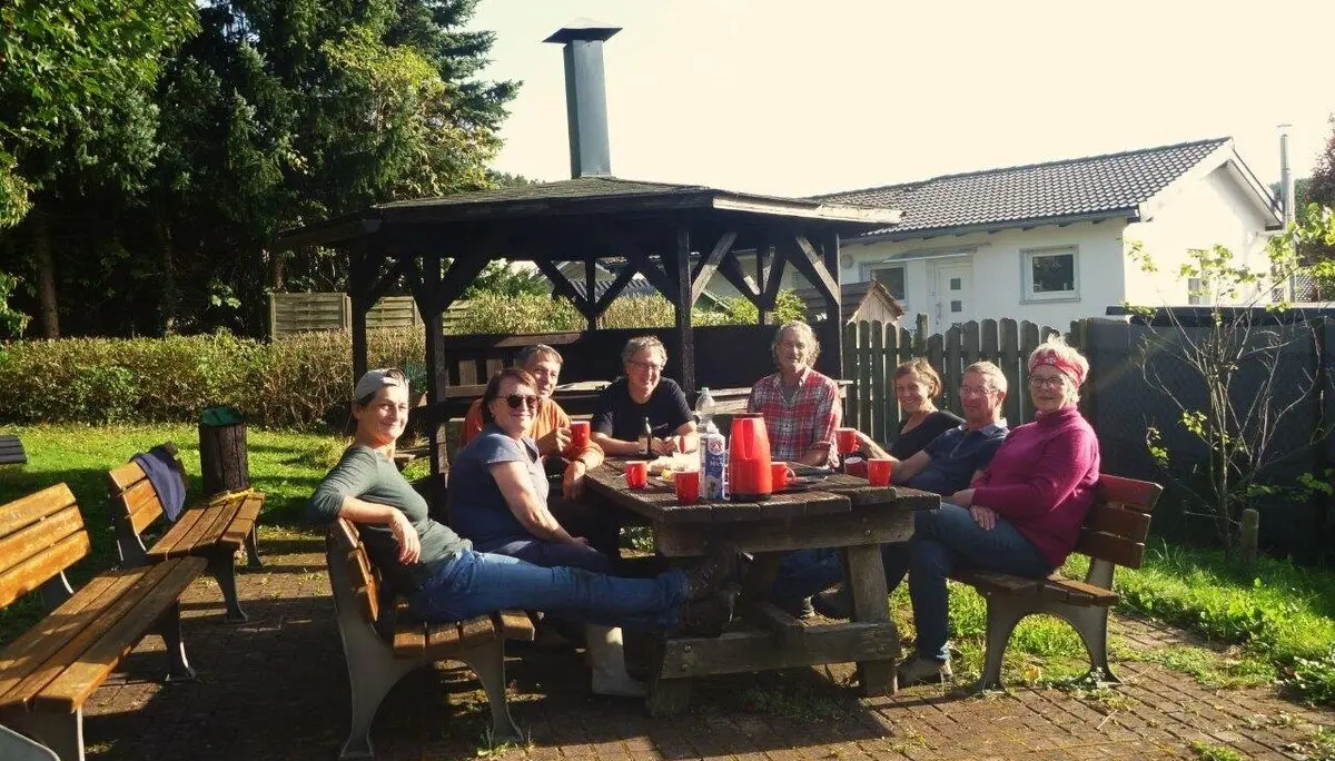 Sieben Personen sitzen gemütlich an einem Gartentisch bei Sonnenschein, Getränke auf dem Tisch. | © DAV Dortmund