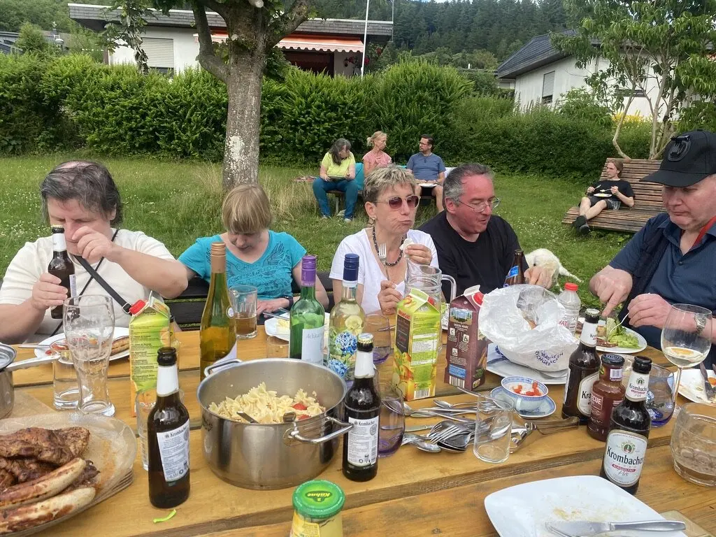 Mehrere Personen sitzen an einem Tisch im Garten und essen gemeinsam. Es gibt Würstchen, Nudelsalat, Getränke und verschiedene Soßen. | © DAV Dortmund