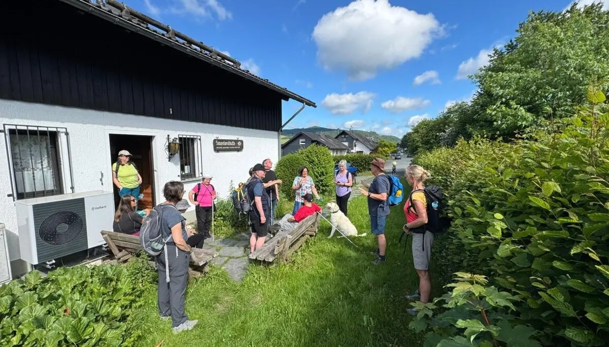 Die Gruppe steht bei Sonnenschein vor einem weißen Gebäude mit dem Schild „Sauerlandhütte“, ein blinder Teilnehmer sitzt mit Hund auf einer Bank. | © DAV Dortmund