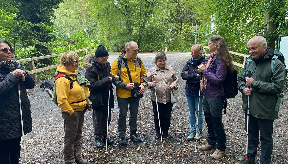 Eine Gruppe von acht Personen mit Wanderstöcken steht auf einem Waldweg. Sie unterhalten sich und tragen Outdoor-Kleidung. Die Umgebung ist grün und naturbelassen. | © DAV Dortmund