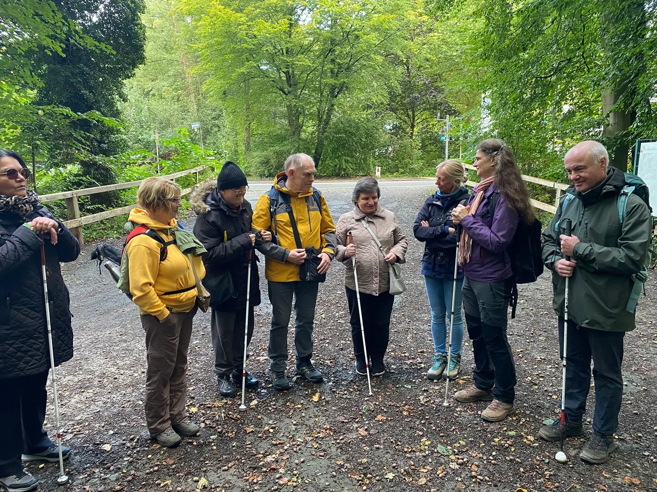 Eine Gruppe von acht Personen mit Wanderstöcken steht auf einem Waldweg. Sie unterhalten sich und tragen Outdoor-Kleidung. Die Umgebung ist grün und naturbelassen. | © DAV Dortmund