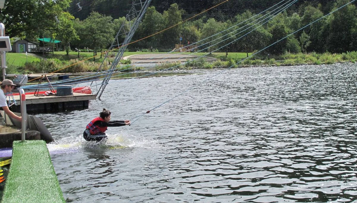 Eine Person beginnt mit dem Wasserskifahren an einer Seilzuganlage am Seeufer. | © DAV Dortmund