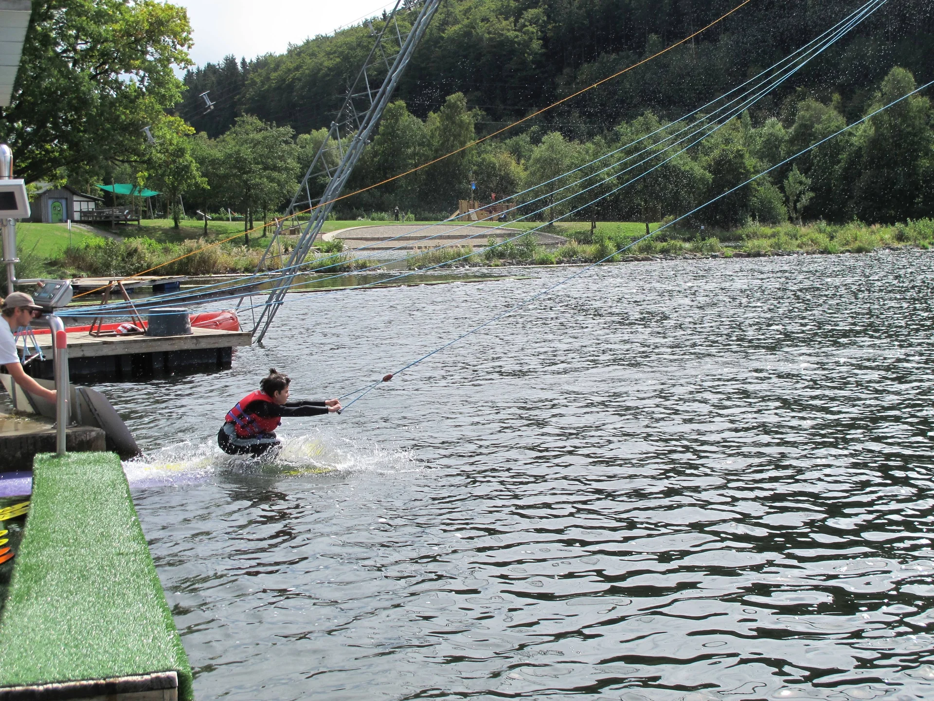 Eine Person beginnt mit dem Wasserskifahren an einer Seilzuganlage am Seeufer. | © DAV Dortmund