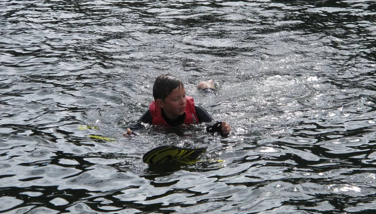Ein Kind mit roter Schwimmweste schwimmt im See und hält sich an den Wasserskiern fest. | © DAV Dortmund
