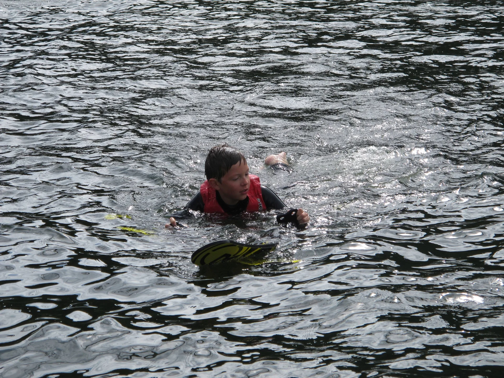 Ein Kind mit roter Schwimmweste schwimmt im See und hält sich an den Wasserskiern fest. | © DAV Dortmund