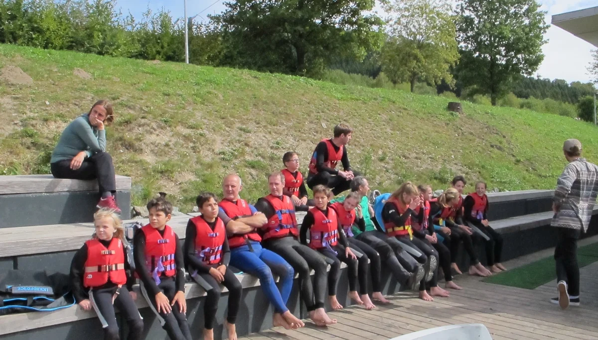 Jugendliche mit Neoprenanzügen und Schwimmwesten sitzen auf einer Holztribüne an einer Wassersportanlage. | © DAV Dortmund